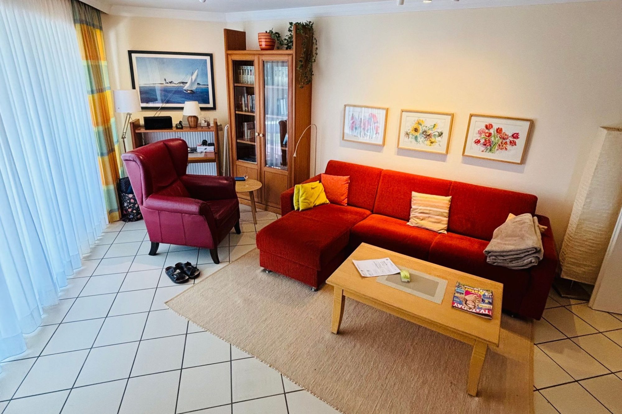 Wohnung 3 Heller Wohnraum mit rotem Sofa, Holztisch und TV-Schrank, dekoriert mit Bildern.