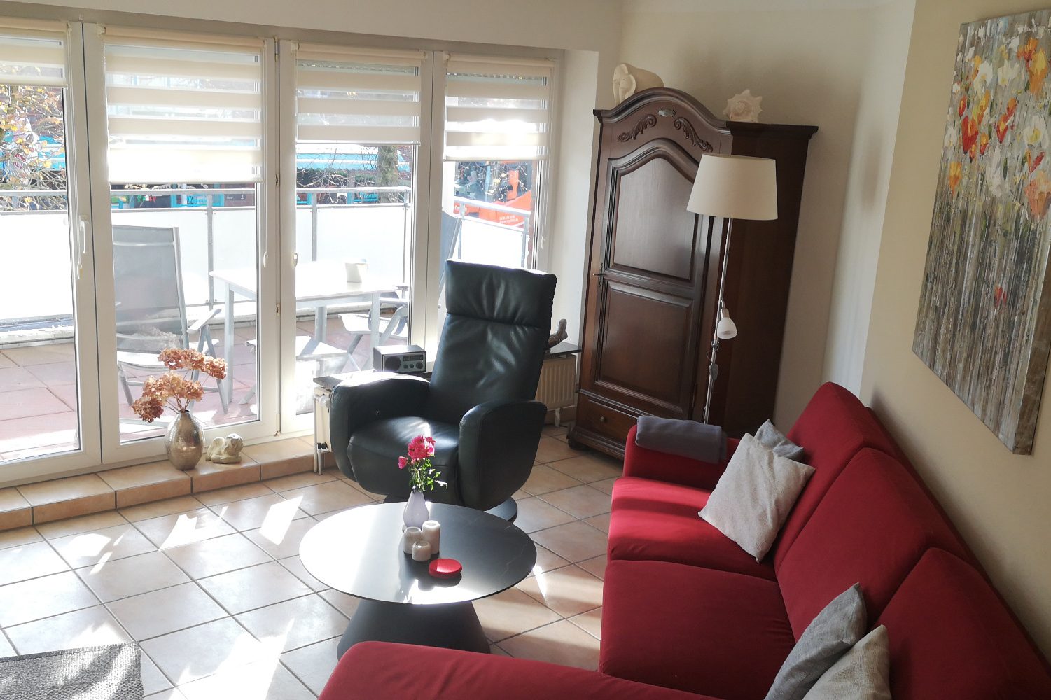 Wohnung 6 Helle Wohnsitzecke mit rotem Sofa, schwarzem Sessel und großem Fenster.