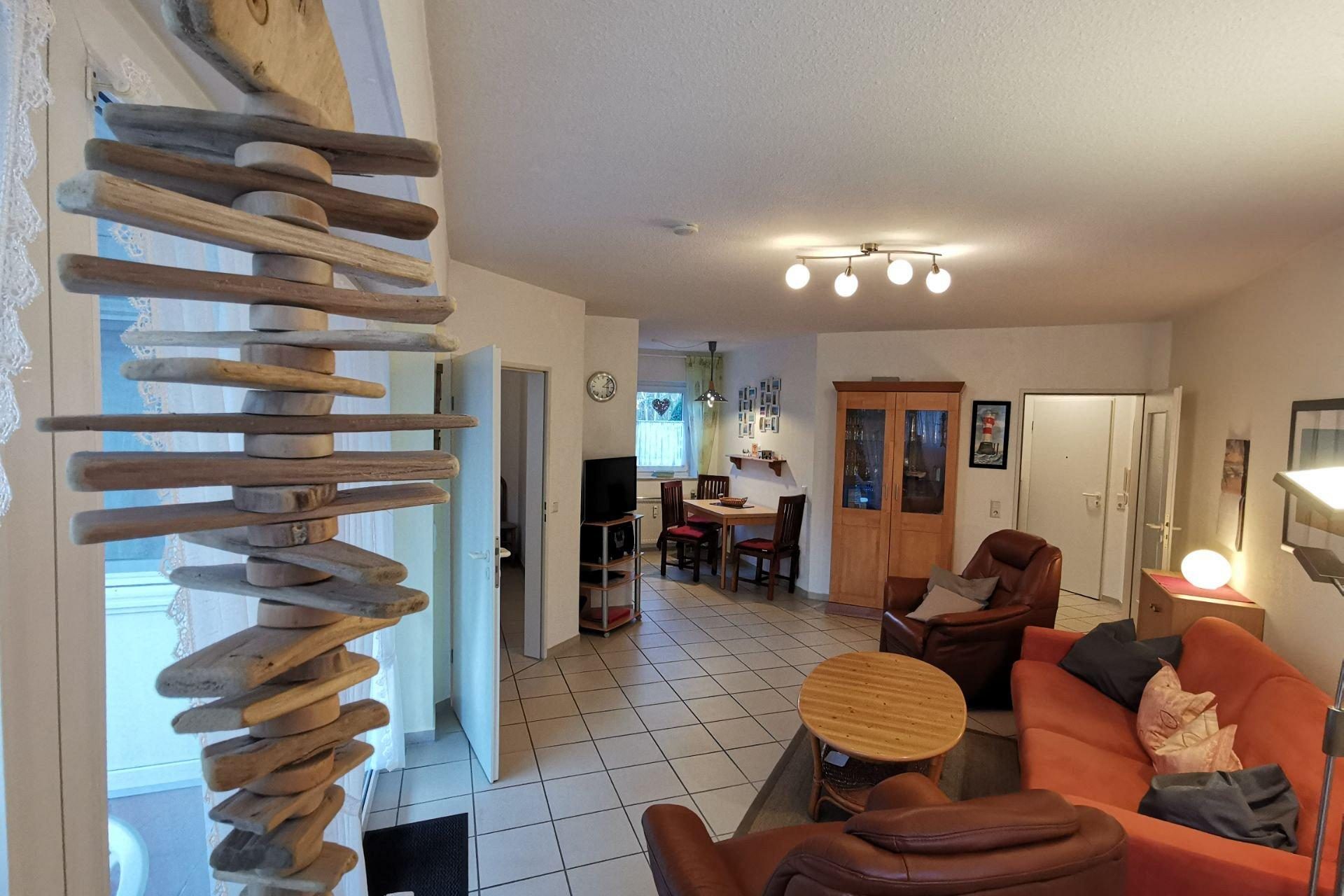 Wohnung 1 Wohnzimmer mit rotem Sofa, zwei Sesseln und Kaffeetisch, hellen Wänden und Bildern.