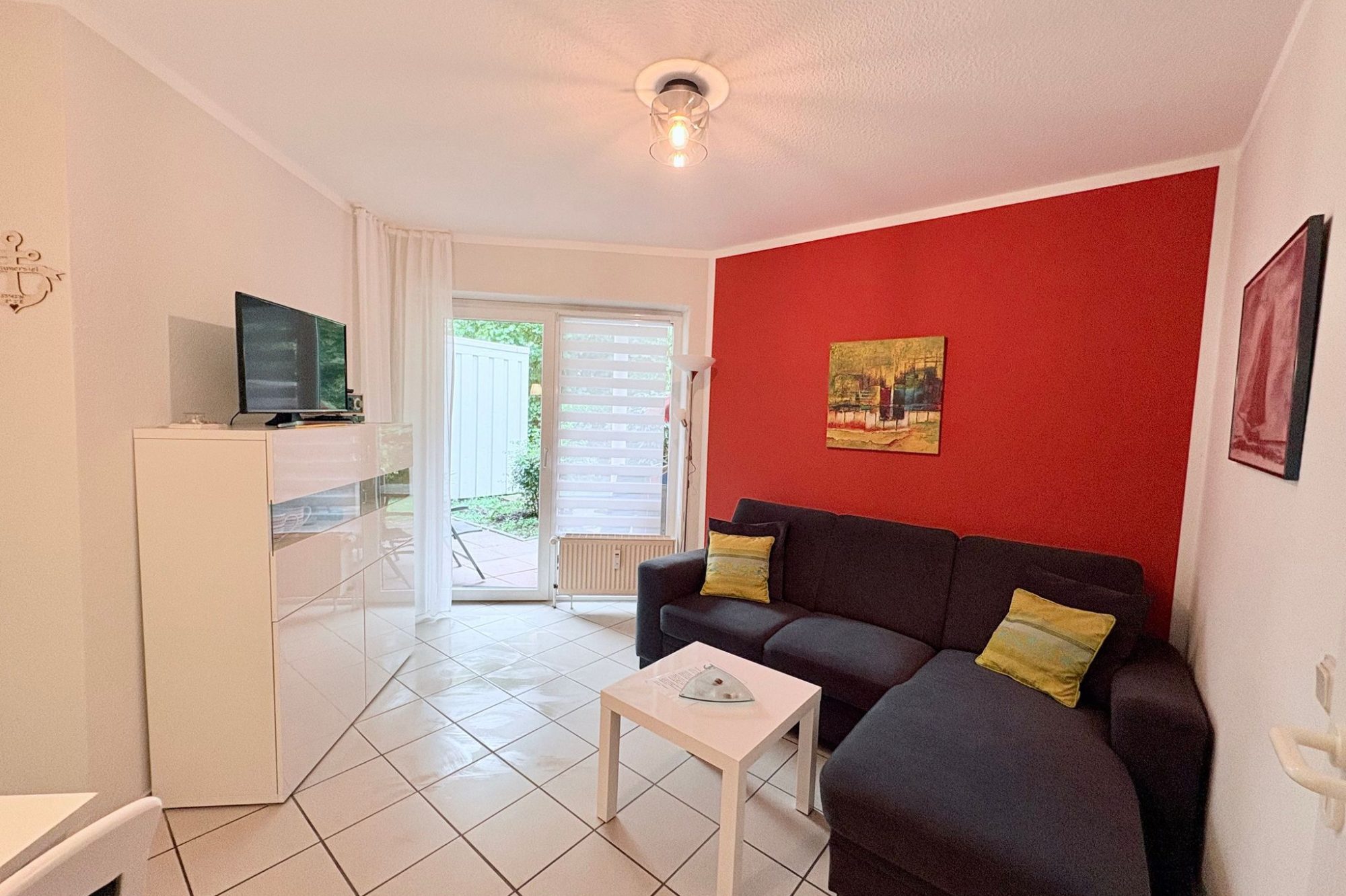 Wohnung 2 Wohnzimmer mit roter Wand, schwarzem Sofa, einem Tisch und einem offenen Küchenbereich.