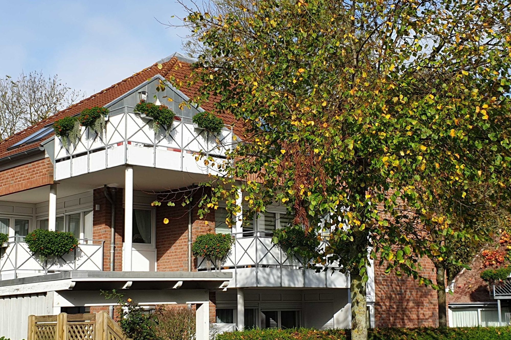 FAQ Zweifamilienhaus mit Balkon, umgeben von Bäumen und buntem Laub.