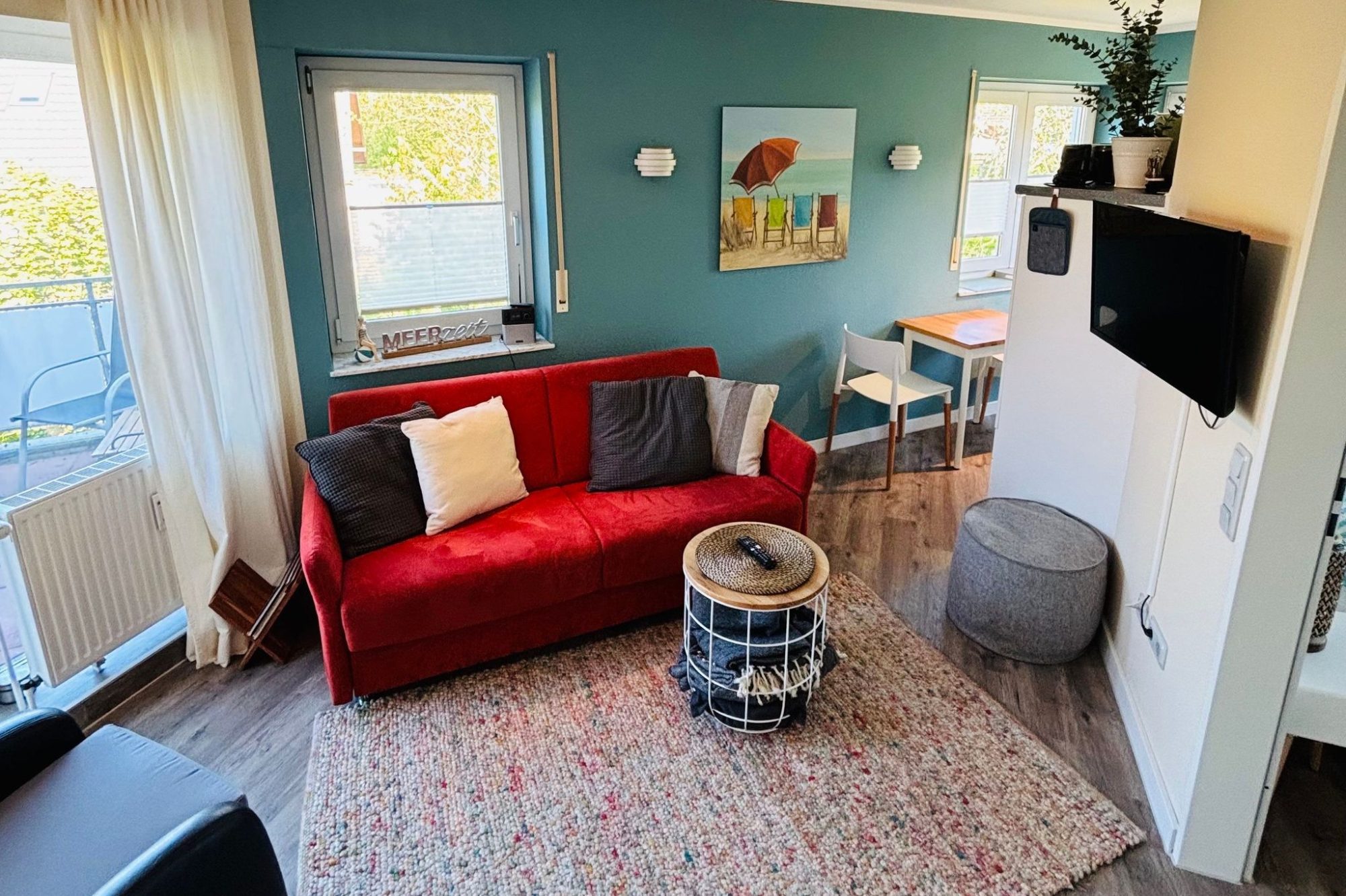 Wohnung 5 Heller Wohnbereich mit rotem Sofa, schwarzen Sessel und Zugang zur Terrasse.