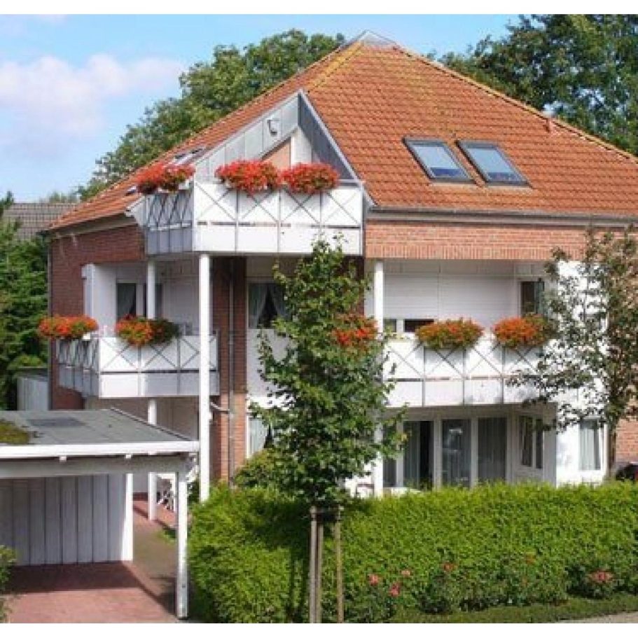 Unsere Wohnungen Drei Etagen Wohnhaus mit roten Blumenbalkonen und einem Garten.